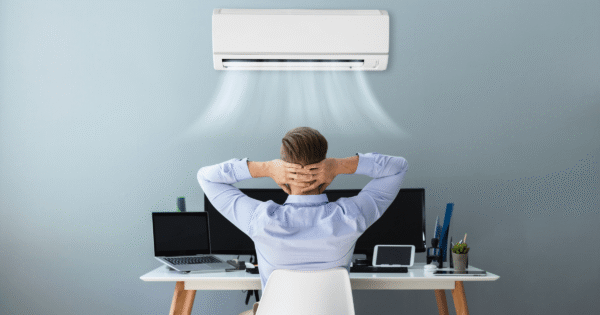 Professional preventative air conditioning maintenance - a man relaxing in front of a working AC unit in a modern office.