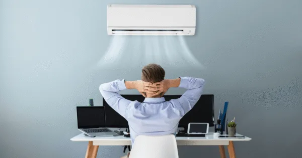 Professional preventative air conditioning maintenance - a man relaxing in front of a working AC unit in a modern office.