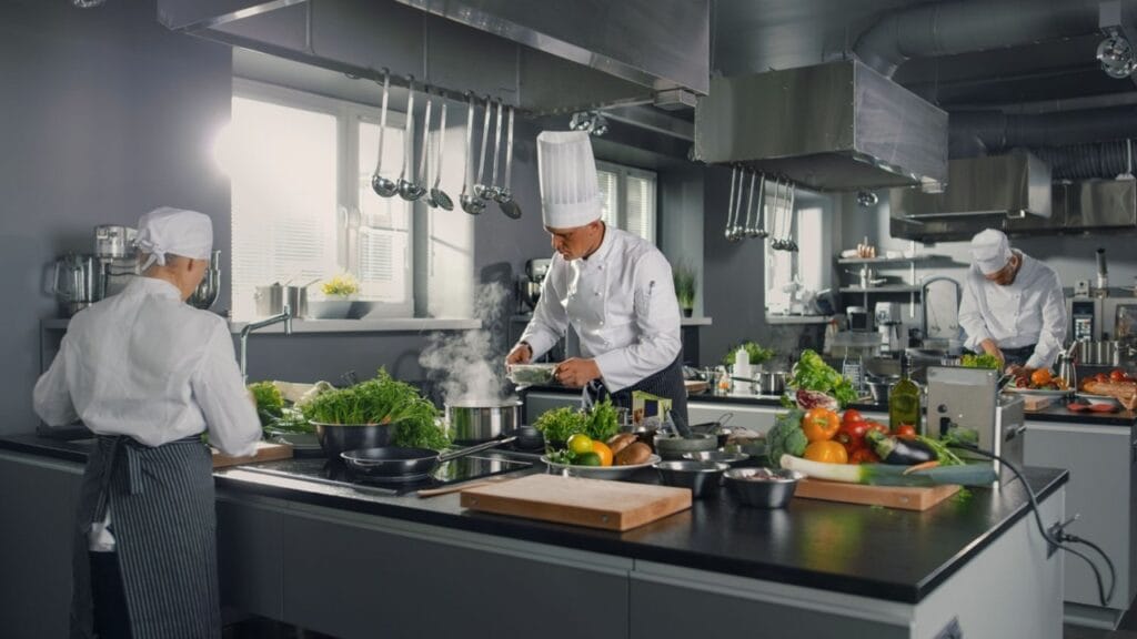 Commercial kitchen with chefs working under industrial HVAC ductwork, essential AC for restaurant kitchen ventilation.