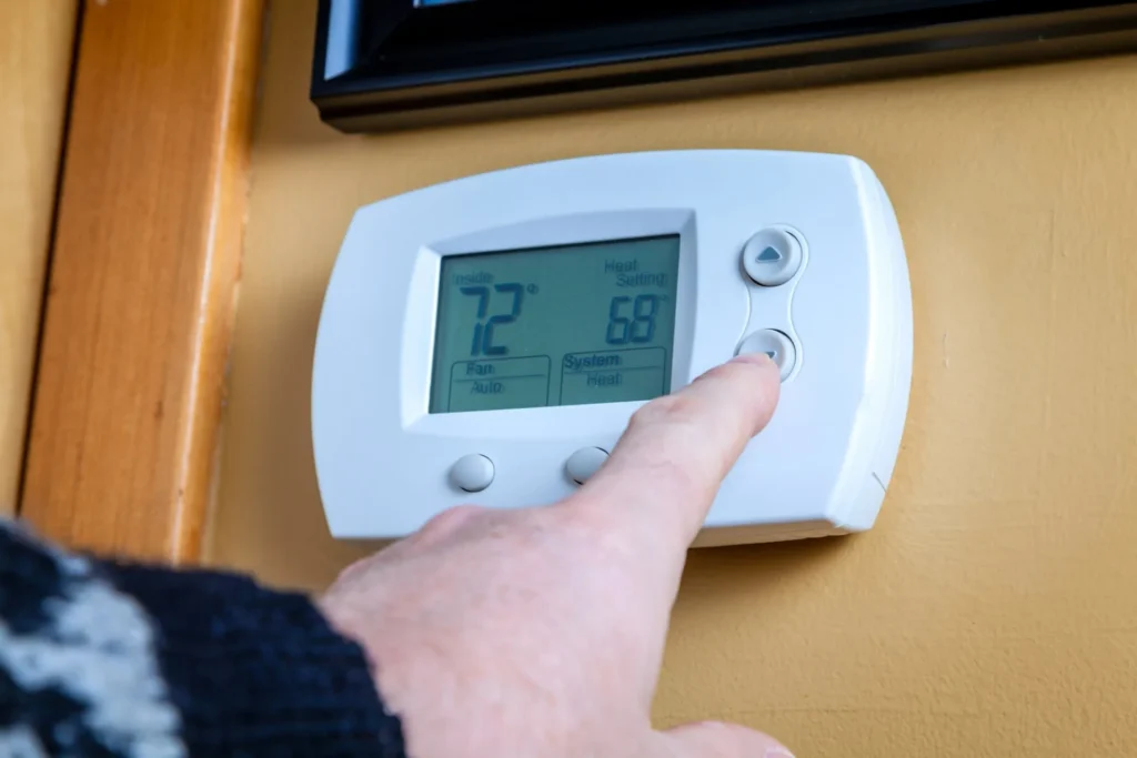 Finger pressing a button on a dimly lit thermostat, showing someone getting ready to turn off HVAC when it isn’t heating in air conditioning Gold Coast.