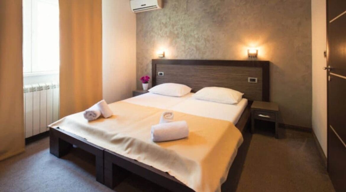 Cozy hotel room with wall-mounted air conditioner above the bed, representing the benefits of AC in hotel rooms for guest comfort and restful sleep.