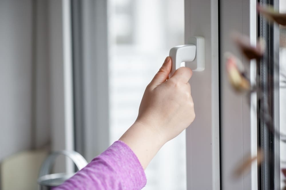 Hand opening a white window handle, symbolizing the broader question of whether to leave doors open or closed for airflow.