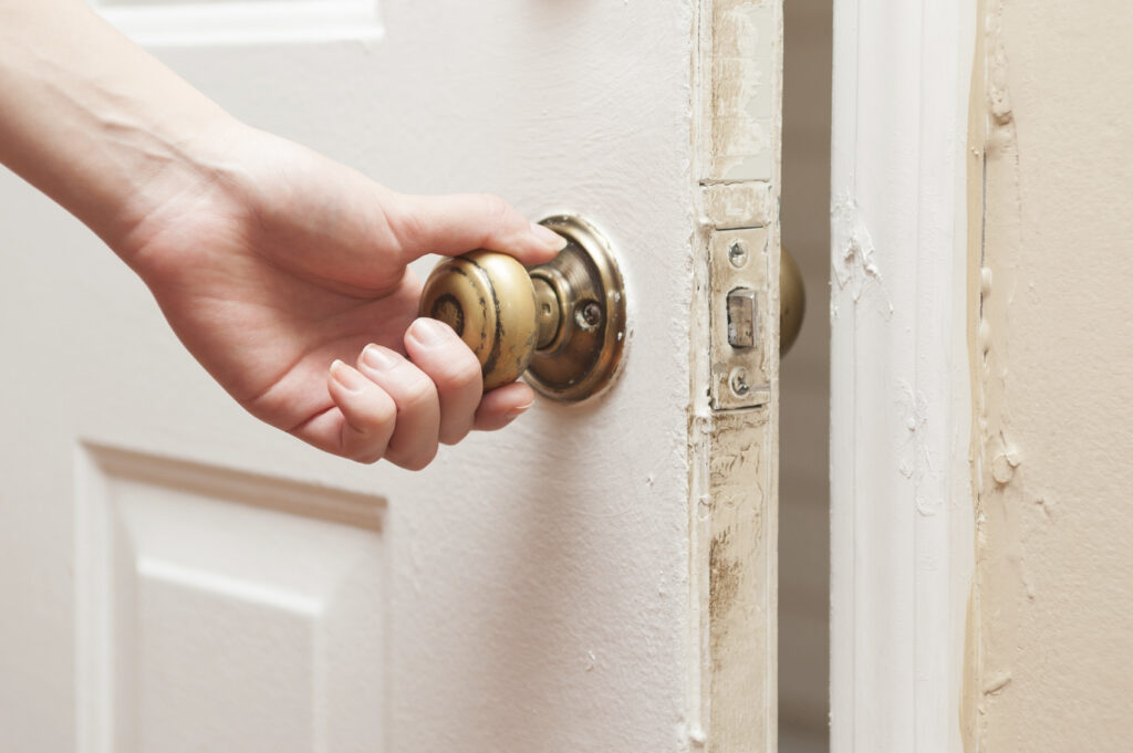 Close-up of a hand turning an old brass doorknob on a partially opened door, representing the decision to leave doors open or closed in home settings.