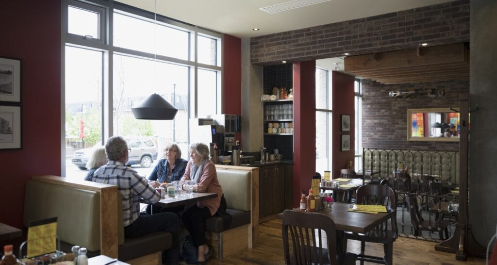 Cozy restaurant interior with guests dining near large windows, where consistent temperature for a restaurant is essential for comfort.