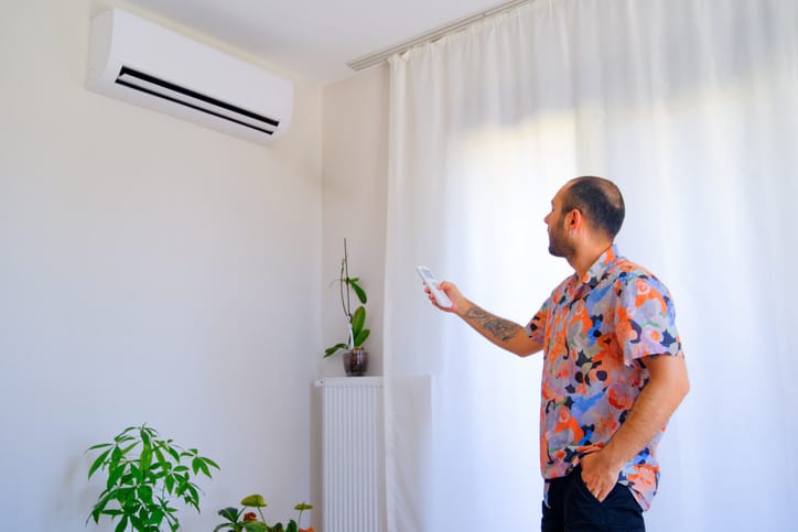 Man using remote control to turn on air conditioning in Gold Coast home with Econo mode for efficiency.