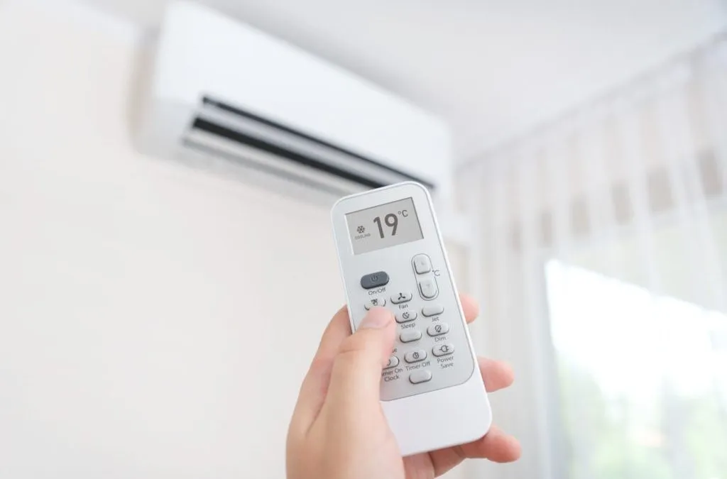 Setting air conditioner to 19°C using a wireless remote for cool indoor comfort.