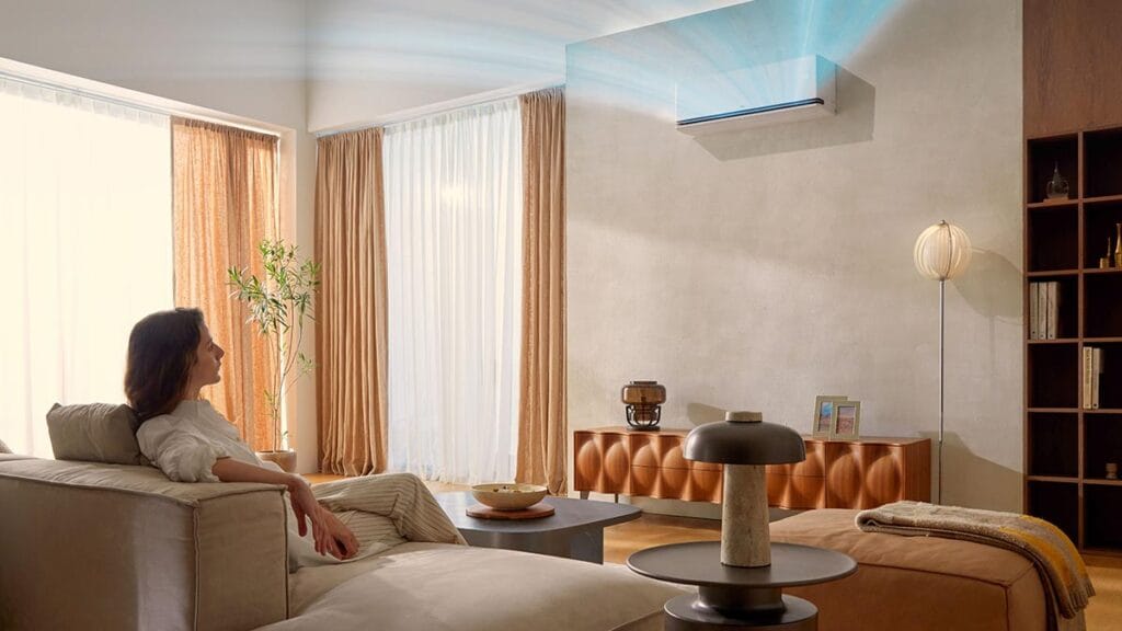 Woman relaxing on a sofa while enjoying the cool breeze from an LG DualCool AI Air conditioner in a bright living room with natural light and warm-toned curtains.