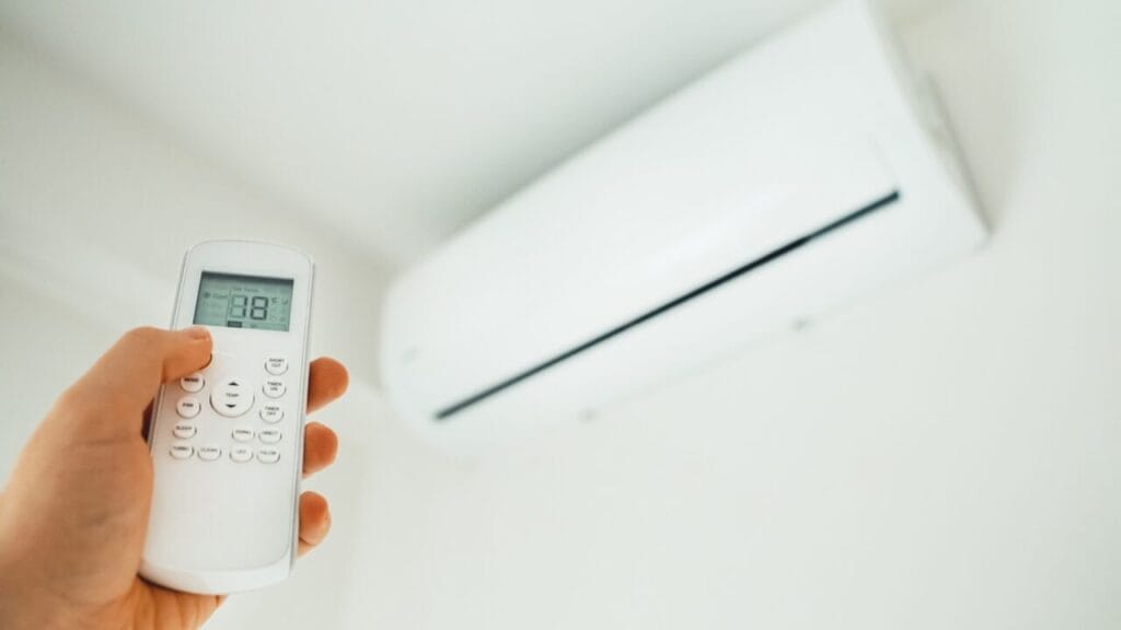 Person holding an AC remote in front of a wall-mounted air conditioner, exploring hidden features in your AC remote.