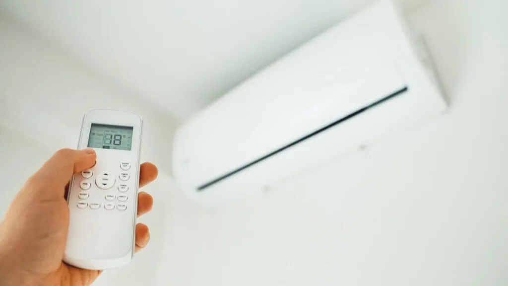 Person holding an AC remote in front of a wall-mounted air conditioner, exploring hidden features in your AC remote.