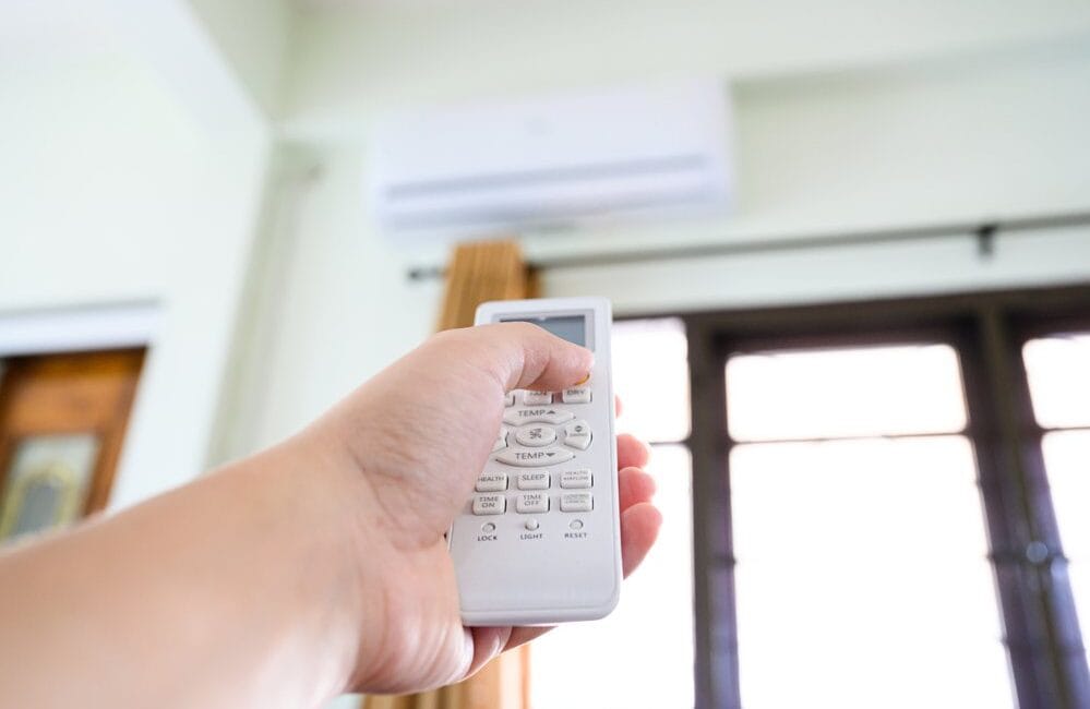Close-up of a hand holding a remote control to turn AC up when they're not home.