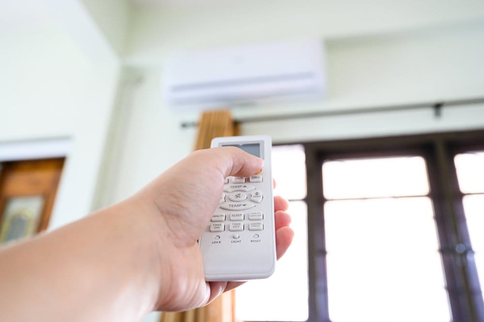 Close-up of a hand holding a remote control to turn AC up when they're not home.