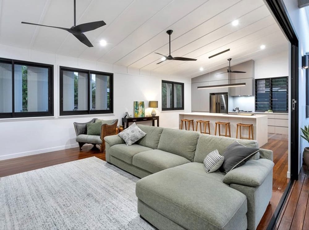 Bright living area with windows, featuring an air conditioner and a ceiling fan, showing how using a ceiling fan while the air conditioner is on uses significantly less energy.