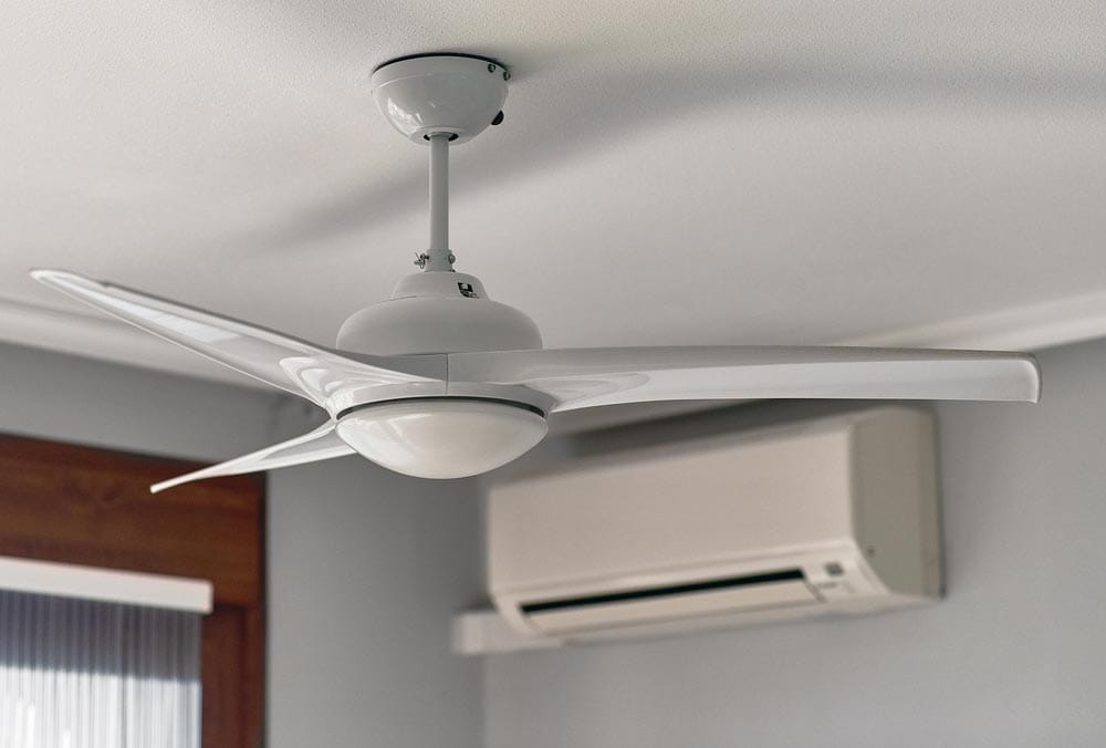 Cozy living space with a modern ceiling fan running alongside the air conditioner, illustrating the key idea: use a ceiling fan while the air conditioner is on to save energy.