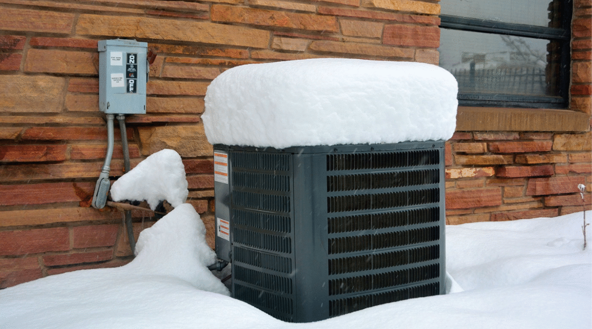 A snow-covered air conditioning unit sits idle outside a brick house during heavy winter snowfall — a reminder of the importance to maintain an AC during winter for homes in regions like the Gold Coast.