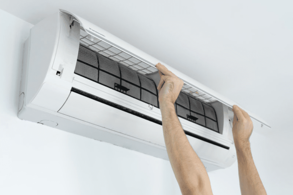 Hands opening the AC unit to check filters due to aircon light blinking when turned on, which may require air conditioning repair.
