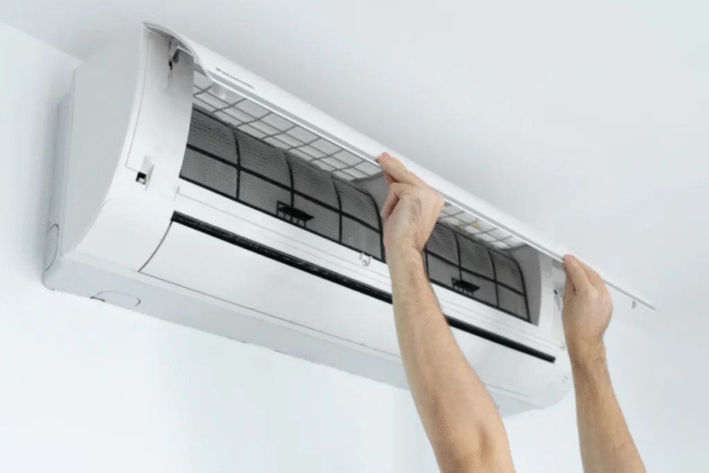 Hands opening the AC unit to check filters due to aircon light blinking when turned on, which may require air conditioning repair.
