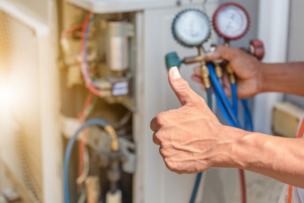 Technician giving a thumbs-up after checking pressure gauges during aircon servicing, confirming system performance.