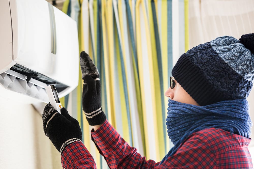 A person in winter clothes trying to warm up with the best heating air conditioner, ideal for unpredictable Gold Coast winters. Get help from an expert air conditioning contractor Gold Coast.