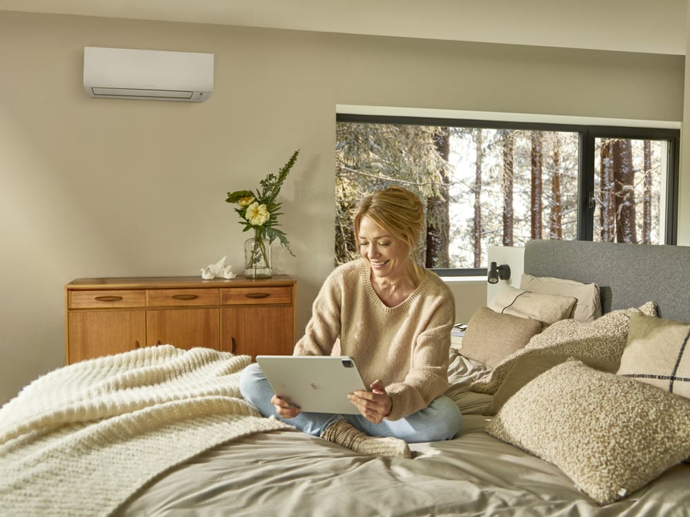 A woman enjoys a warm, cosy bedroom thanks to a reverse-cycle air conditioner—an efficient way to heat your home during winter.