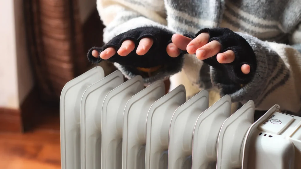 Hands warming up over an electric heater, showing heating mistakes like relying on inefficient portable units.