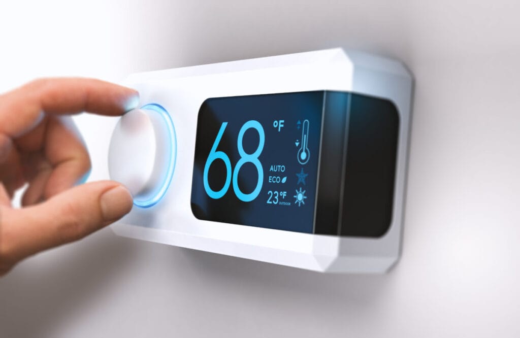 Hand adjusting a smart thermostat to 68°F to turn down the heat before leaving home in winter.
