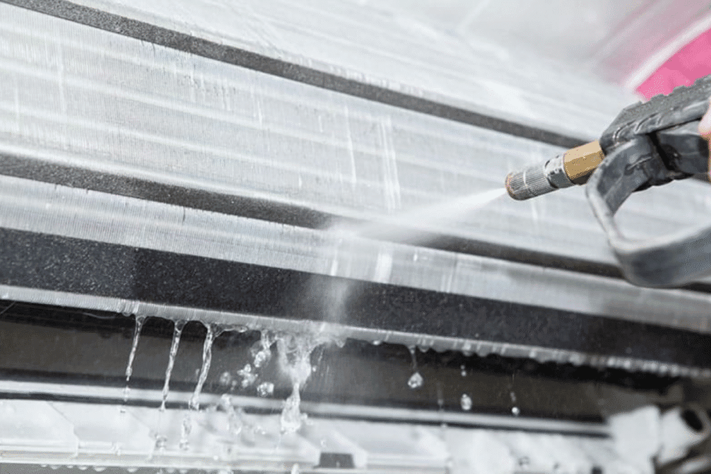Close-up of a technician performing an aircon clean using Hydro Clean chemical clean method on an indoor unit coil, showing water spray removing dirt – air conditioning Gold Coast service.
