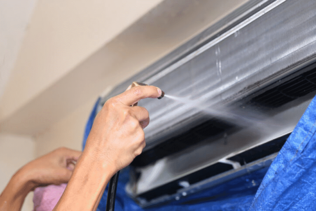 Technician performing Hydro Clean on air conditioner coil using pressure spray, showcasing professional aircon cleaning service on the Gold Coast.