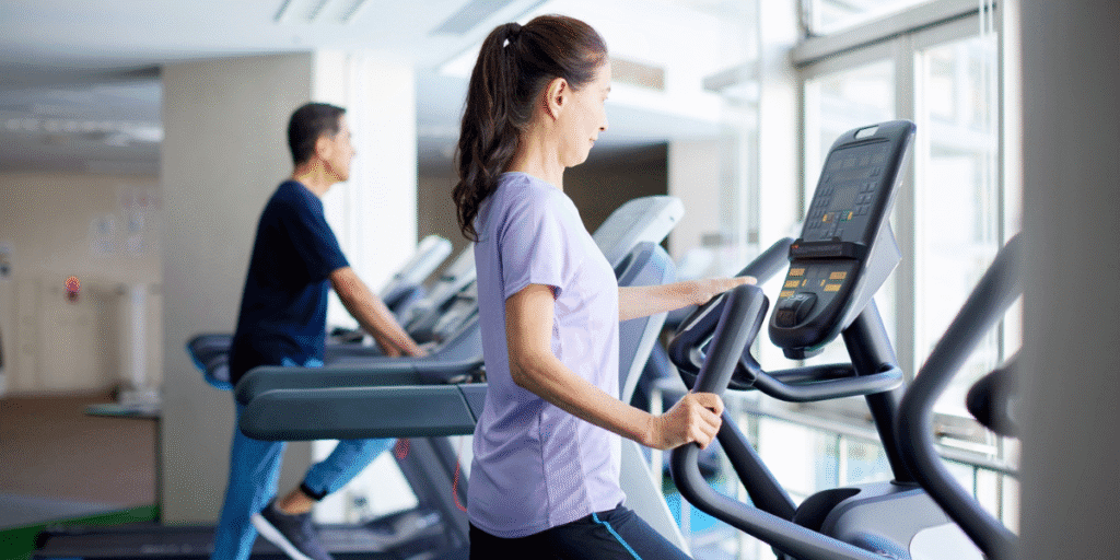 Gym members exercising on cardio machines with visible ceiling vents showing air conditioner placements in gyms, designed by air conditioning Gold Coast experts.