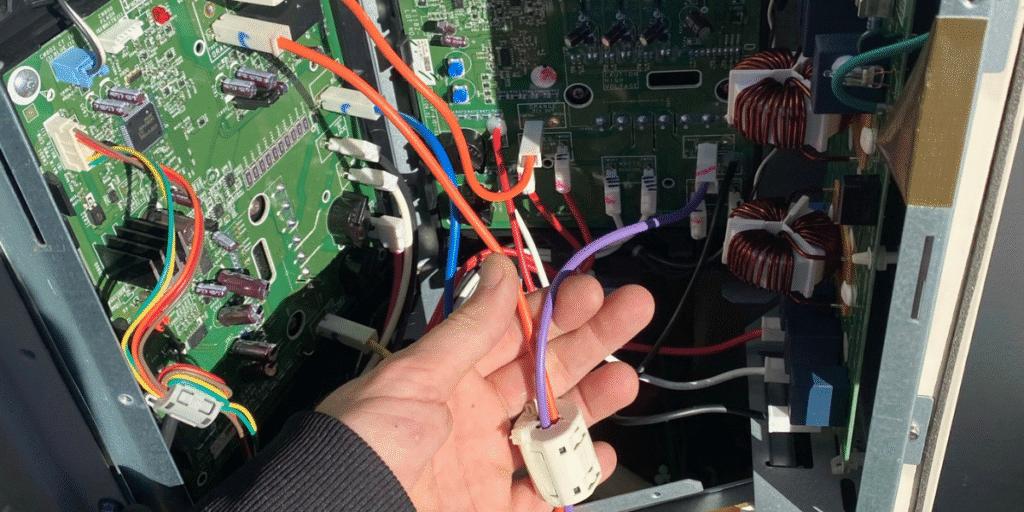 Technician checking circuit board and wiring inside outdoor AC unit – reminder to book preventative maintenance with trusted air conditioning Gold Coast experts.
