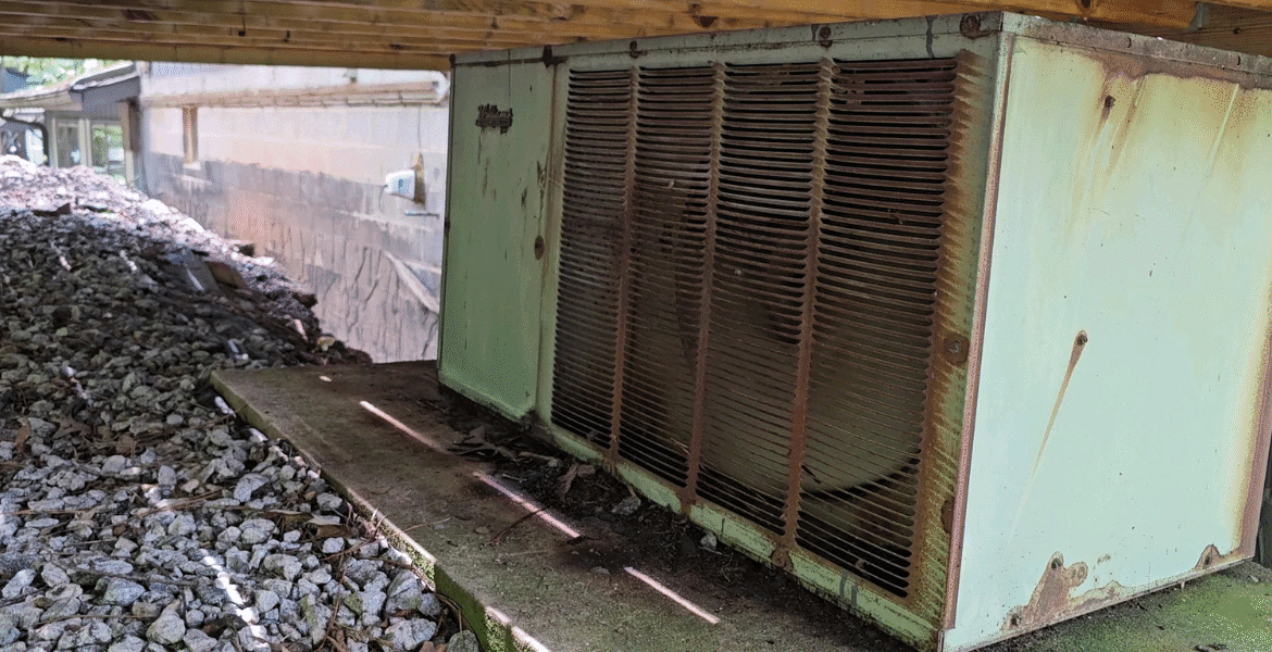 A rusting outdoor air conditioner placed under a house, showing the need to recycle old AC responsibly with air conditioning Gold Coast services.