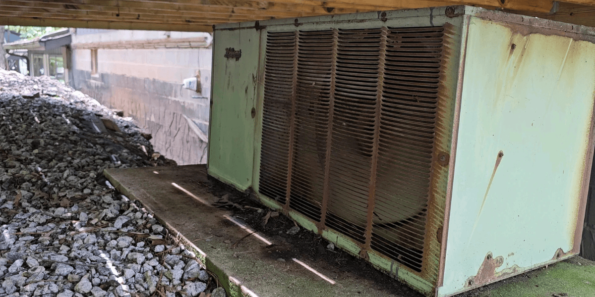 A rusting outdoor air conditioner placed under a house, showing the need to recycle old AC responsibly with air conditioning Gold Coast services.