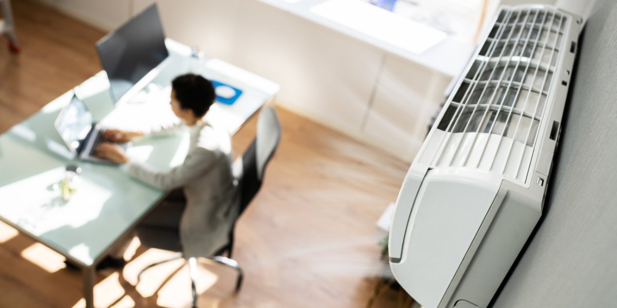 Office worker sitting under a running air conditioner during a heatwave — demonstrating how to avoid thermal shock when using air conditioning in severe weather through proper temperature settings and professional air conditioning Gold Coast maintenance.