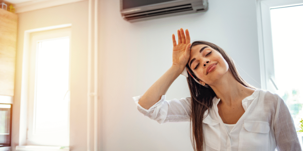 Woman feeling the effects of extreme heat indoors before turning on the air conditioner, illustrating the importance of using air conditioning Gold Coast systems properly during hot weather.