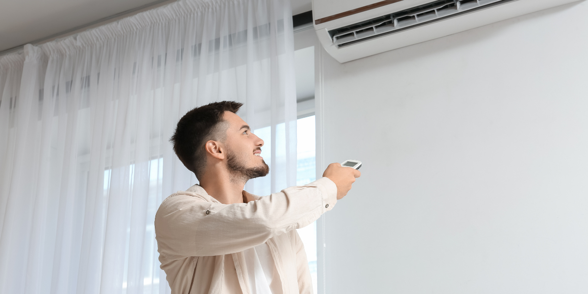 Man adjusting the remote control to set the right temperature for his air conditioner in extreme heat, demonstrating efficient air conditioning Gold Coast usage during high summer temperatures.