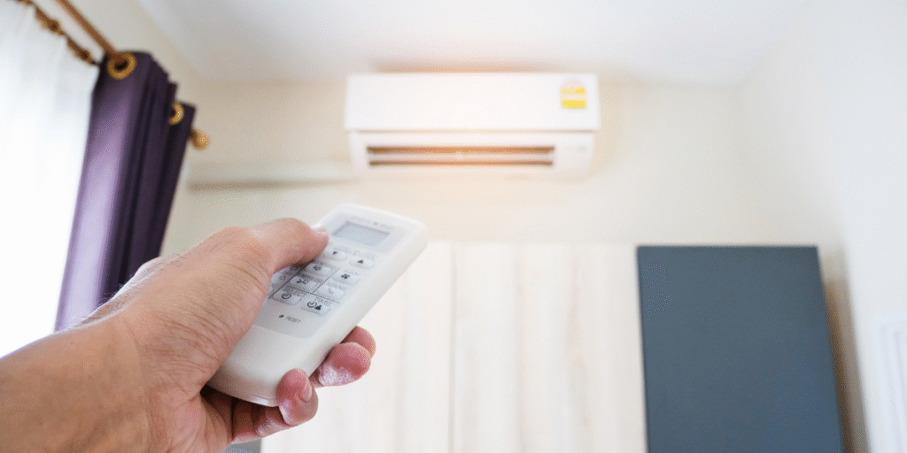 A person using a remote control to adjust an air conditioner that is blowing air but not cooling, illustrating a typical situation for Gold Coast households seeking air conditioning repair service Gold Coast.