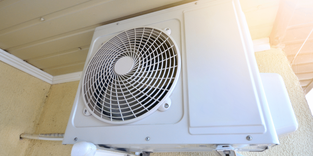Outdoor AC unit mounted under a shaded roof area to protect it from direct sunlight, an example of how to safely cover the outdoor unit without blocking airflow — shared by air conditioning Gold Coast professionals.