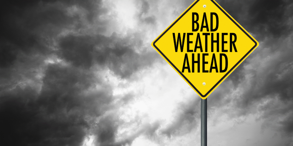 A yellow warning sign reading “Bad Weather Ahead” under dark storm clouds, highlighting the need to prevent air conditioner damage in severe weather across the Gold Coast region.