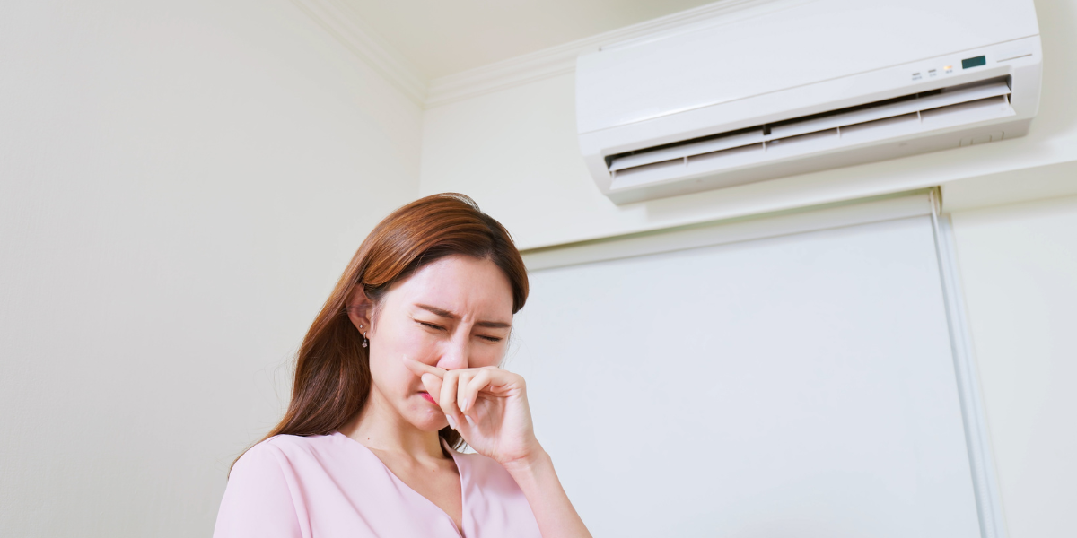Woman reacting to strong air conditioner smell coming from a wall-mounted unit, showing common indoor comfort issues with air conditioning Gold Coast systems.