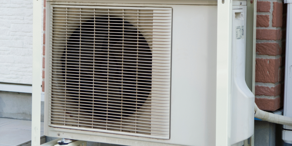 Close-up of a rusty outdoor air conditioner unit installed near a brick wall, showing early signs of corrosion on the casing and fan grille — air conditioning Gold Coast.