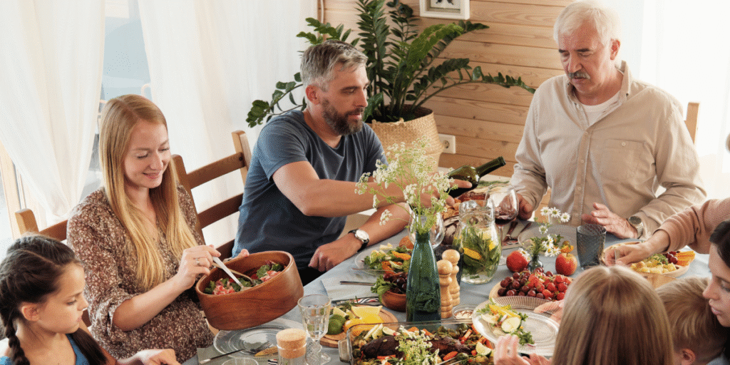 A large family gathered for a meal in a bright dining room, adding body heat and frequent movement that may cause the air conditioner struggle or even overload air conditioner systems, especially in air conditioning Gold Coast homes.