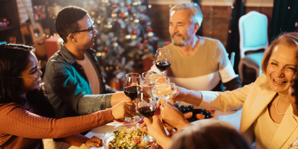 A family raising glasses during a holiday dinner with warm lighting, showing a full house where extra body heat can make the air conditioner struggle, increasing the risk of an overload air conditioner situation for homes using air conditioning Gold Coast systems.