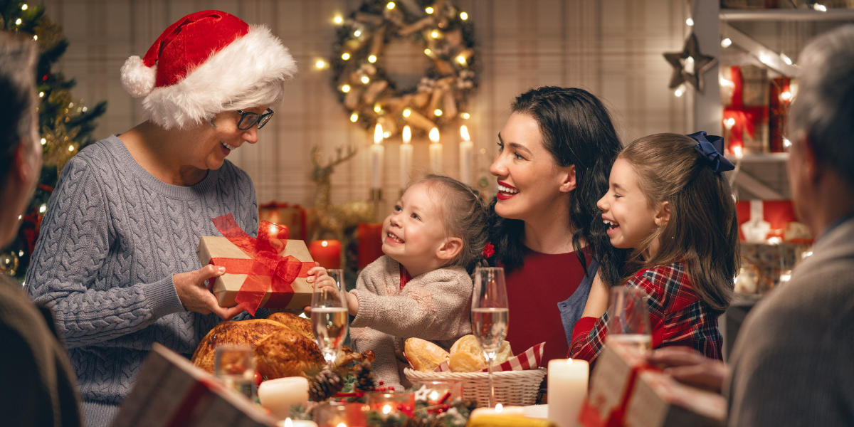 A festive family celebration with children and adults exchanging gifts around a Christmas table, creating extra indoor heat that can make the air conditioner struggle and lead to an overload air conditioner for households relying on air conditioning Gold Coast.