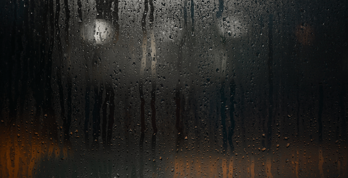 Close-up of water droplets running down a glass window, illustrating severe moisture problems and how humidity affect air conditioner efficiency in air conditioning Gold Coast conditions.