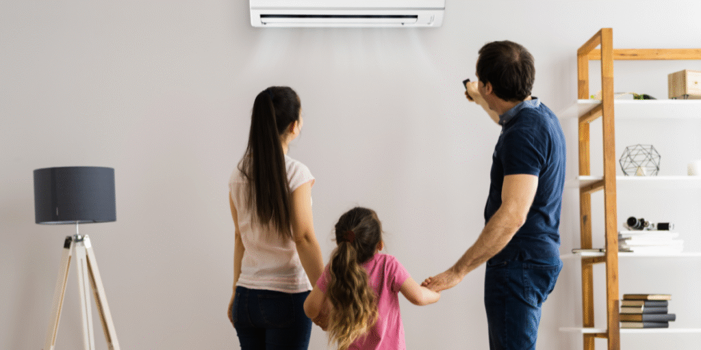 A family standing under a running air conditioner, illustrating household habits of keeping air conditioner below 20°C and how air conditioning Gold Coast experts recommend safer cooling levels.