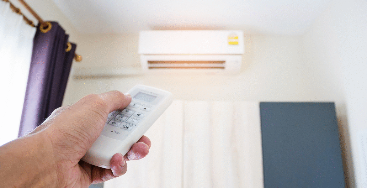A hand holding an AC remote pointed at a running unit, highlighting common habits of leaving your air conditioner all day for cooling stability, a frequent practice in air conditioning Gold Coast households.