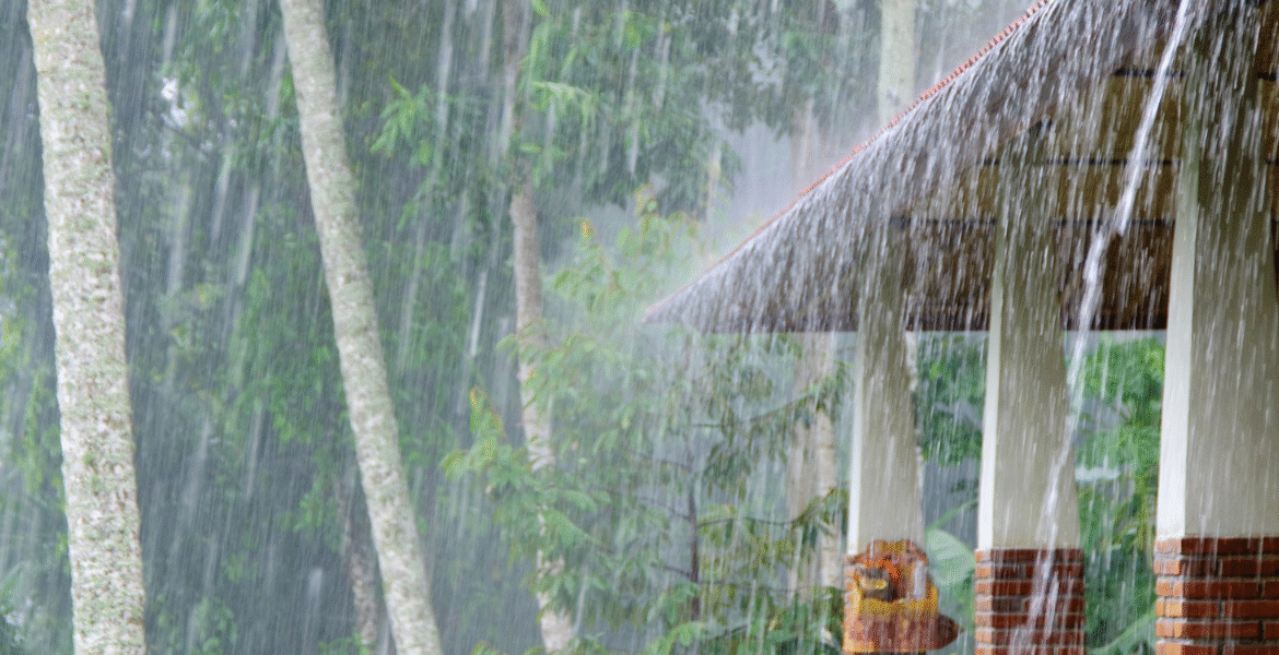 Heavy rainfall on a house roof surrounded by trees, representing storm conditions that can trigger outdoor unit leaking electricity in air conditioning Gold Coast properties.