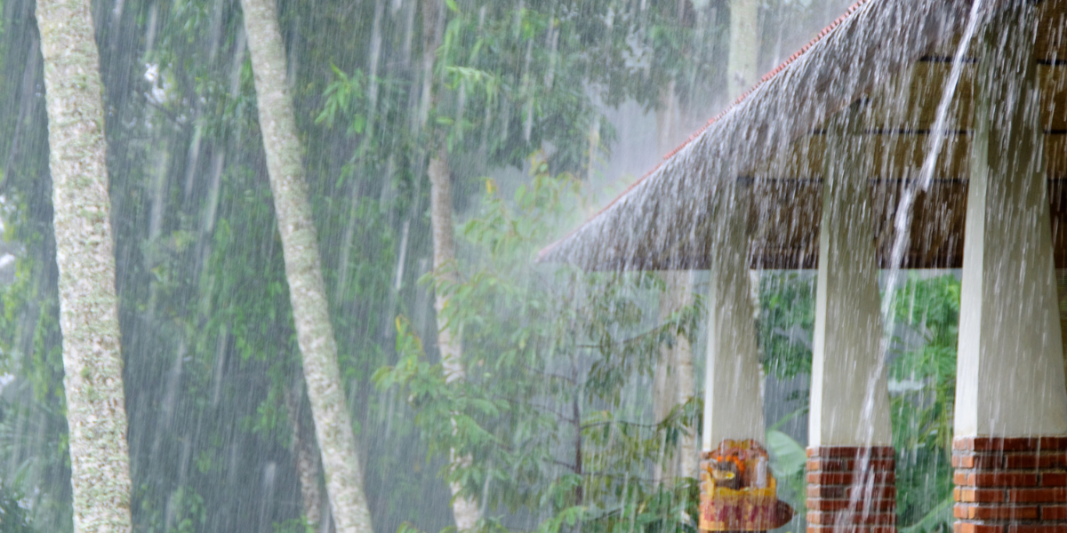 Heavy rainfall on a house roof surrounded by trees, representing storm conditions that can trigger outdoor unit leaking electricity in air conditioning Gold Coast properties.
