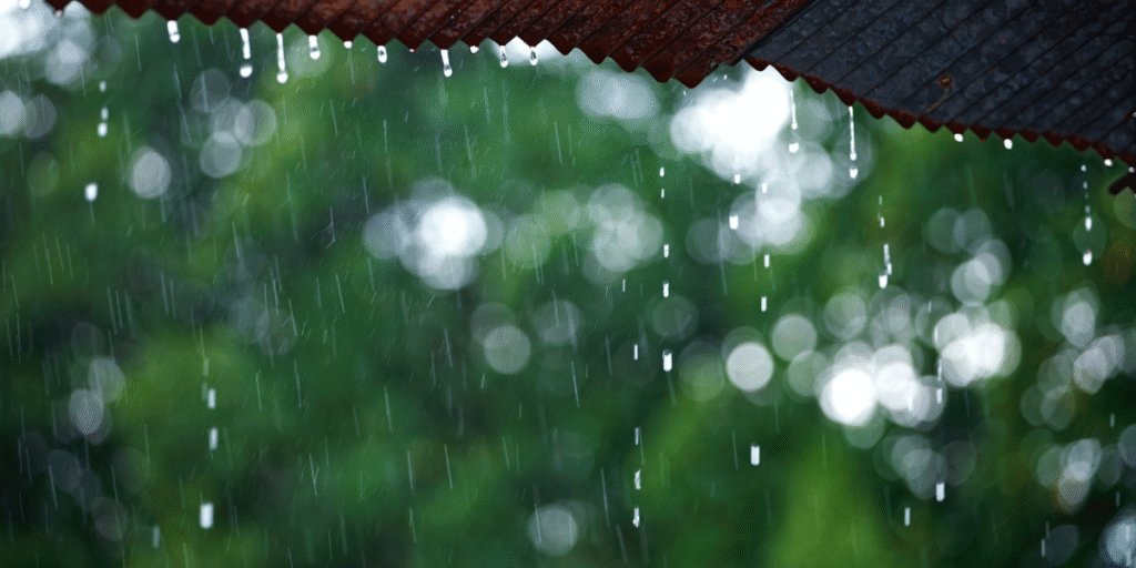 Heavy rain falling from a rusty roof during a tropical storm, showing how extreme weather can affect outdoor air conditioners and cause outdoor unit leaking electricity in air conditioning Gold Coast homes.