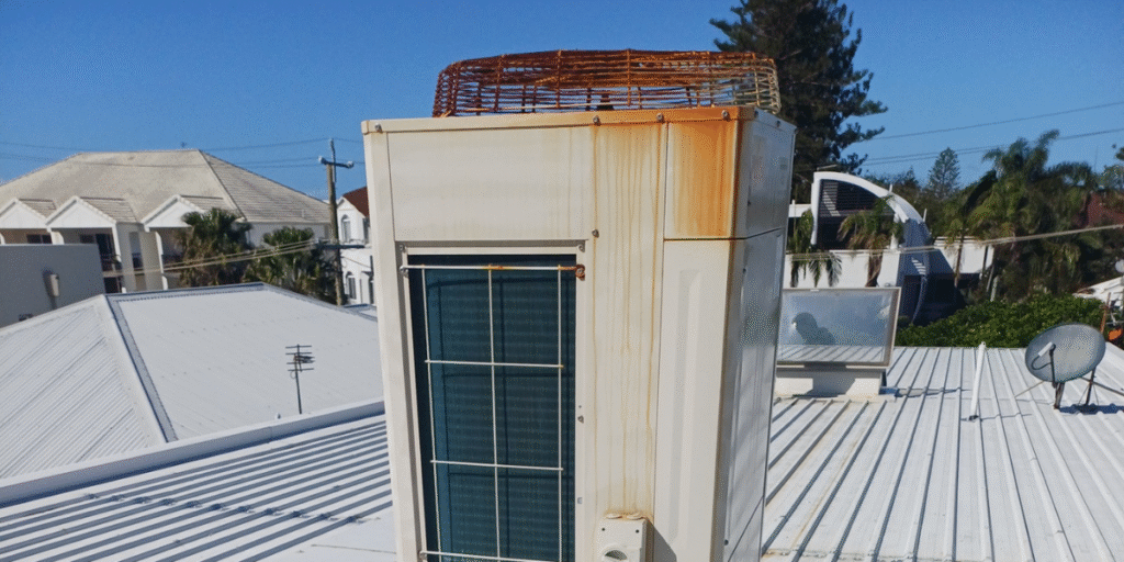 Rusty outdoor air conditioner unit installed on a rooftop, showing corrosion caused by salt and humidity — common in air conditioning Gold Coast systems.