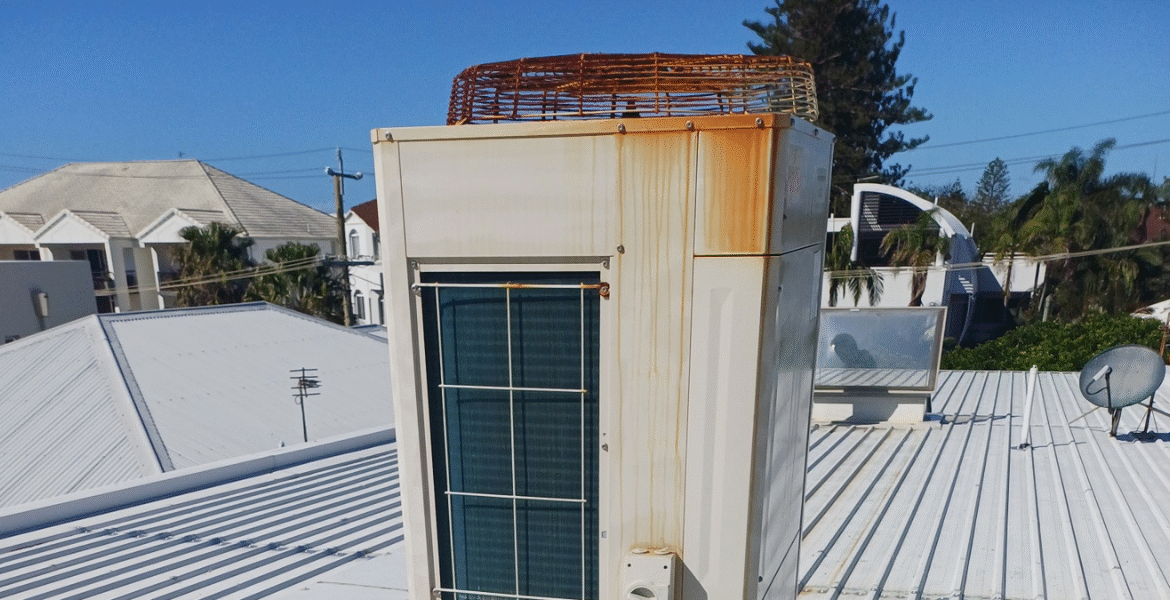 Rusty outdoor air conditioner unit installed on a rooftop, showing corrosion caused by salt and humidity — common in air conditioning Gold Coast systems.